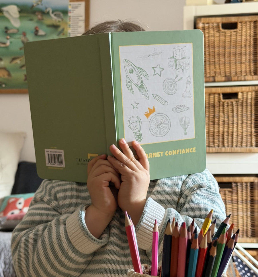 Un enfant tient le carnet Confiance devant son visage